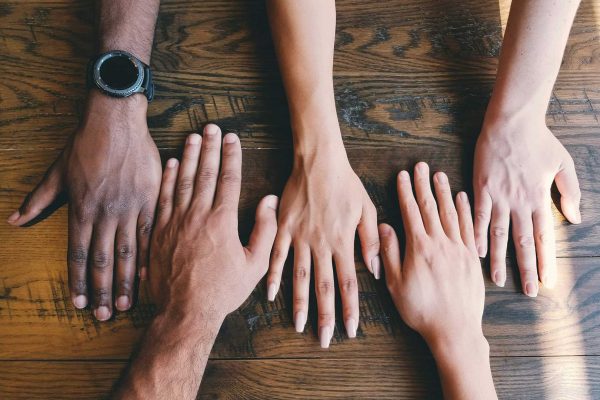 Pessoas de diferentes raças com as mãos sob a mesa representando comunicação inclusiva