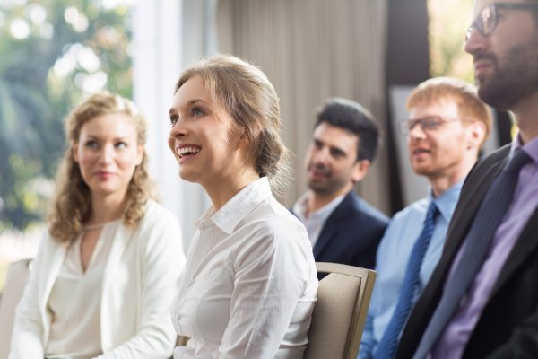 Young businesswoman and her male and female colleagues smiling, sitting and watching presentation in conference room